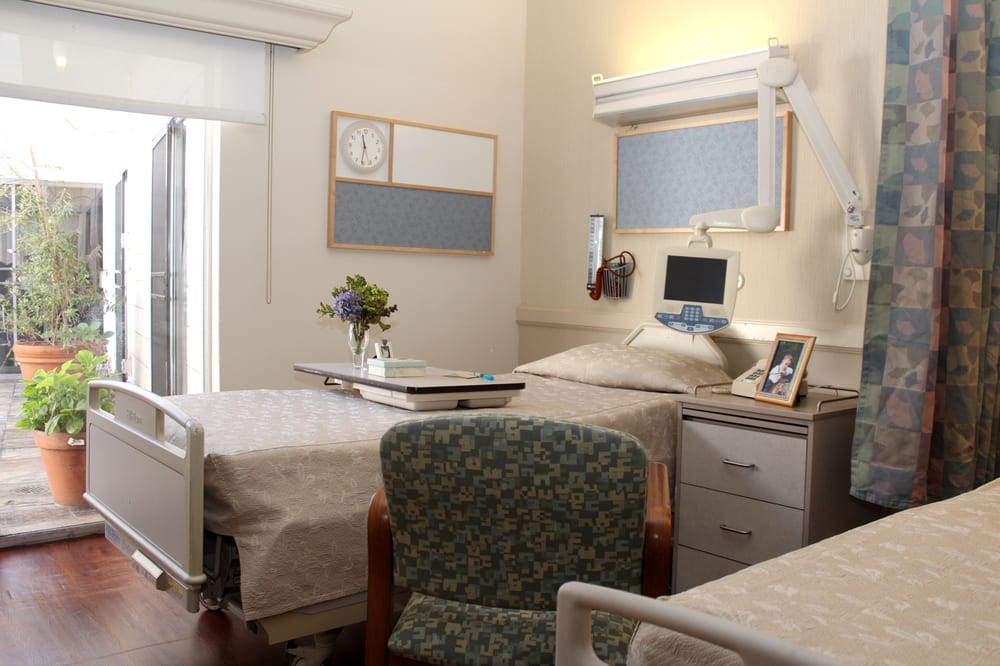 A well-organized hospital room with a bed, chair, and a small table with flowers.
