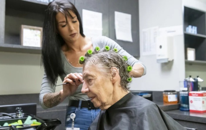 A hairdresser styles an elderly woman's hair in a salon.