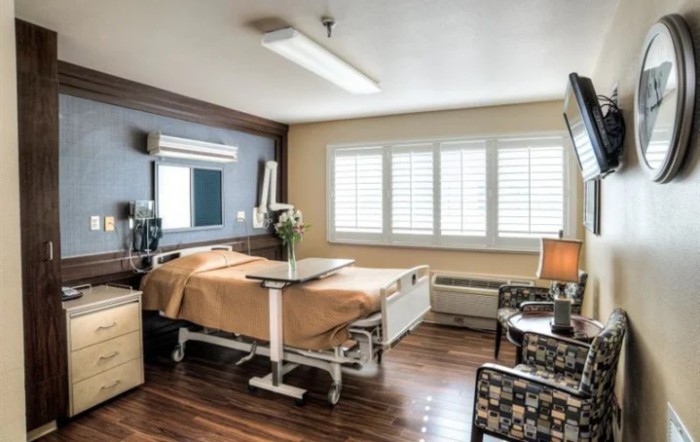 A well-lit hospital room with a bed, medical equipment, and comfortable furnishings.