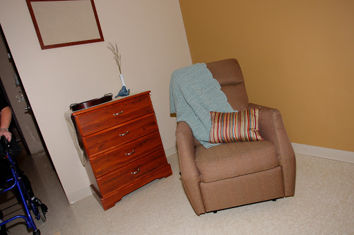 A cozy corner featuring a comfortable chair with a throw blanket and a striped pillow, alongside a wooden drawer chest.
