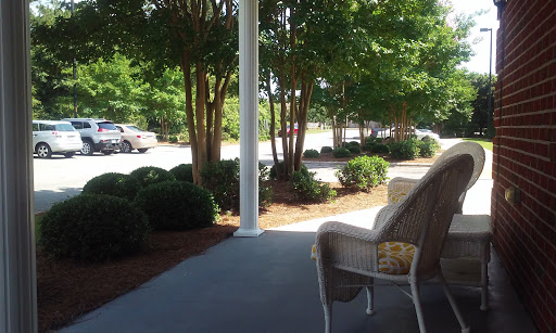 A peaceful view from a porch surrounded by trees and shrubs, with a glimpse of parked cars in the background.