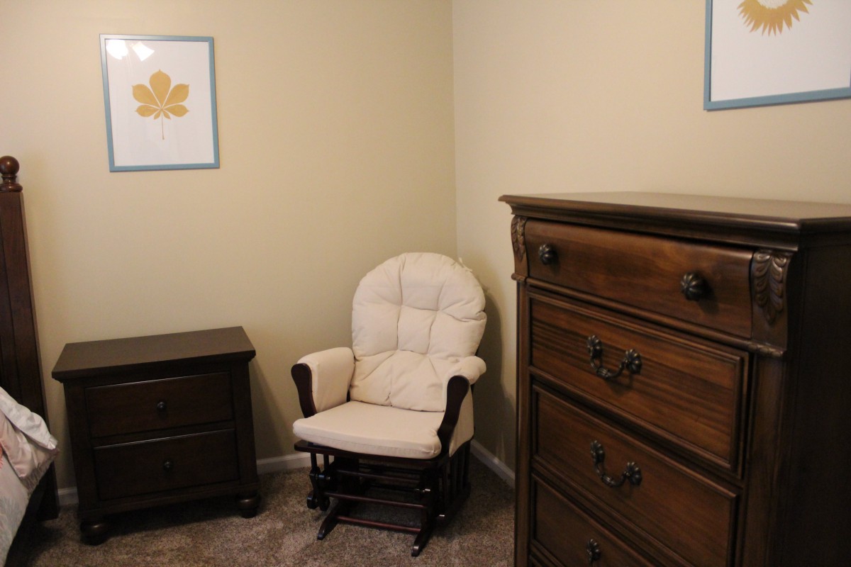 A cozy nursery corner with a cushioned rocking chair and wooden dresser.