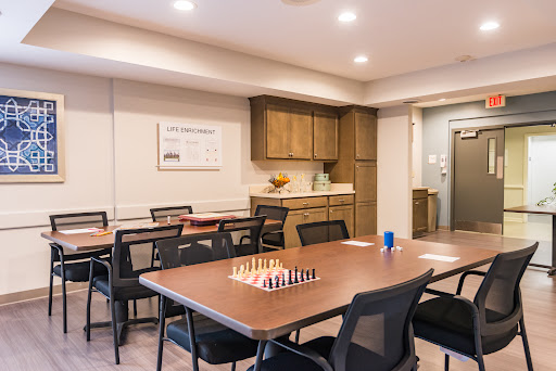A well-lit meeting room featuring a chess set on the table, surrounded by chairs and wooden cabinetry.