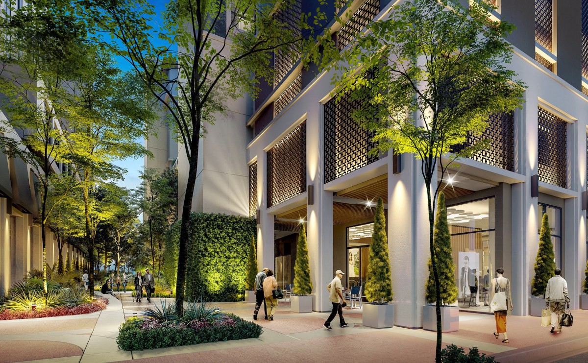 A modern urban building with illuminated architecture and greenery at night, featuring people walking by.
