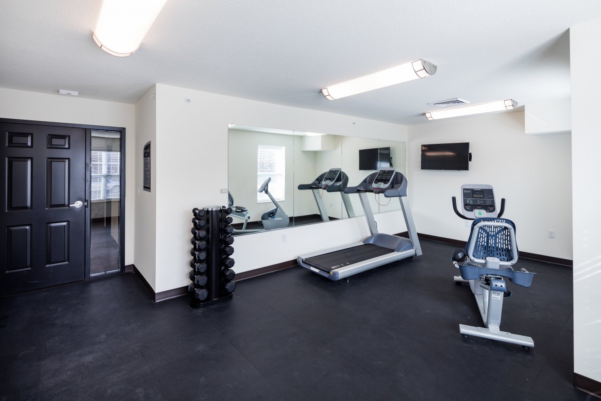 A small gym with treadmills, stationary bike, and dumbbells.