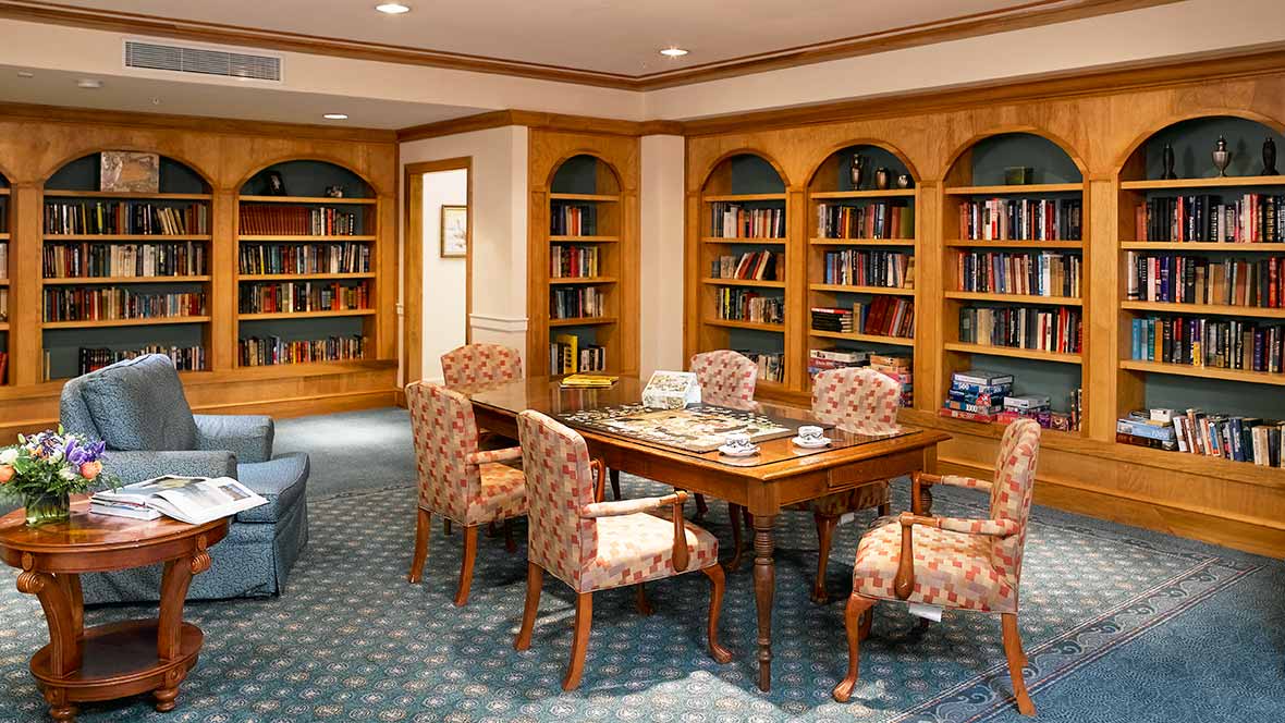 A cozy library reading room with bookshelves, a table, and chairs.