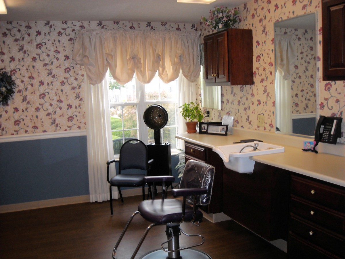 A cozy hair salon with floral wallpaper, a styling chair, and a large window adorned with curtains.