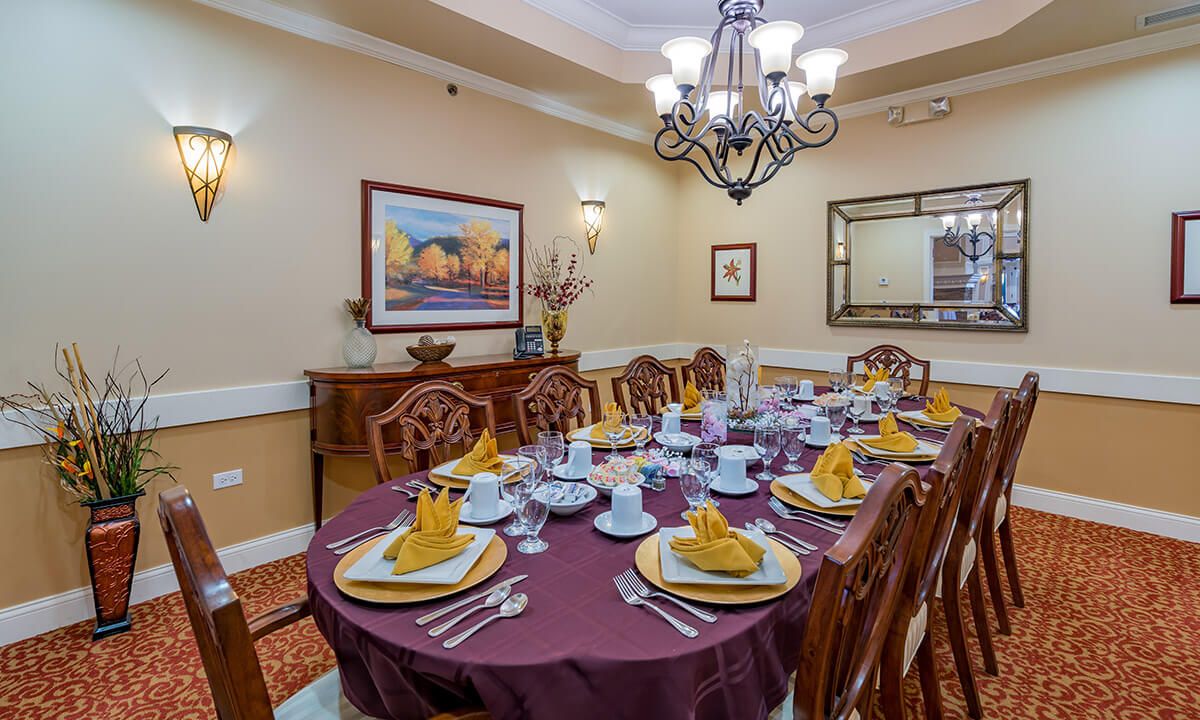 An elegantly set dining room with a chandelier overhead and decorative plates arranged on a table with folded napkins.