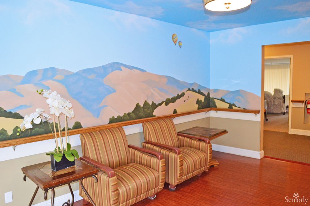 A cozy waiting area with striped armchairs, a mountain mural on the wall, and a wooden floor.