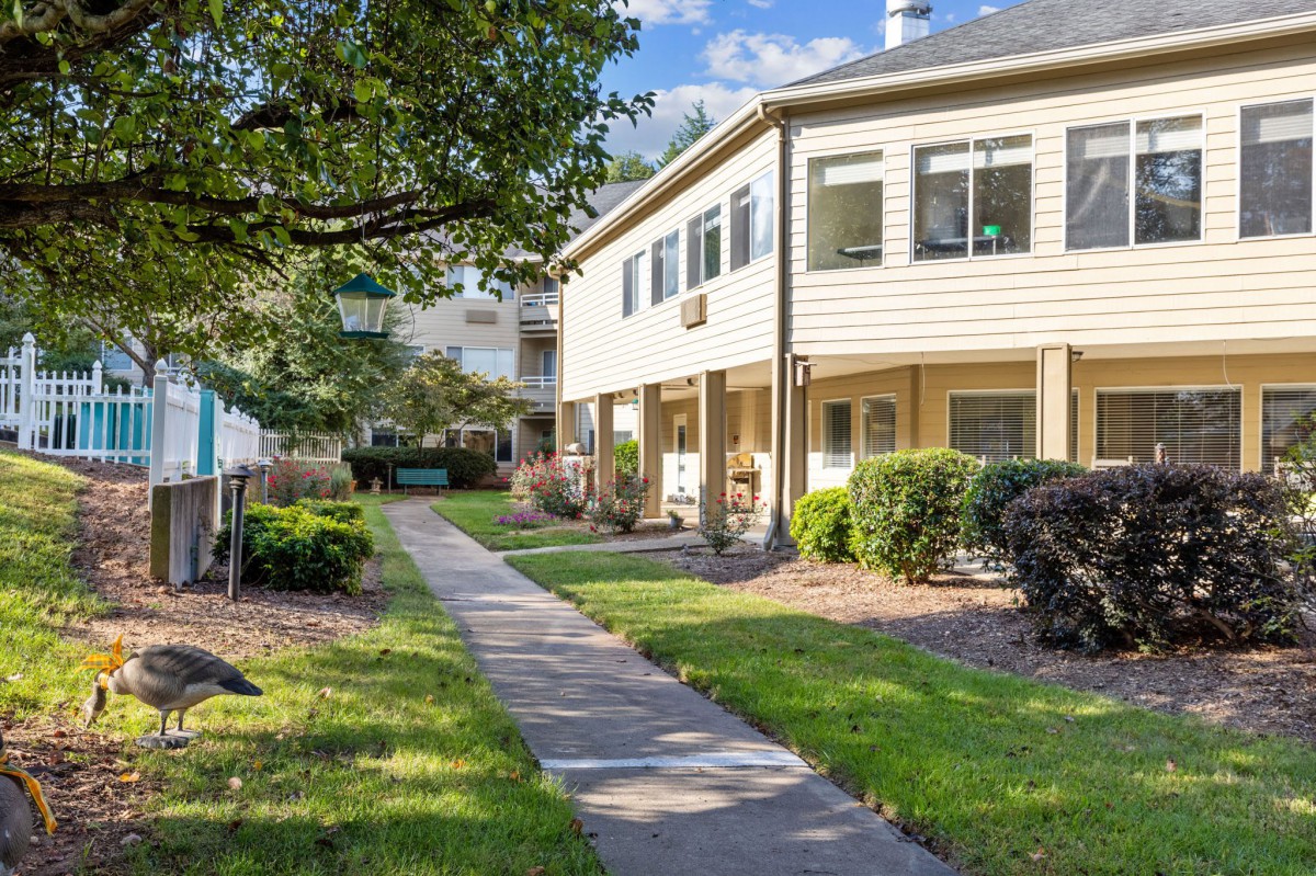 A well-maintained apartment complex with a landscaped yard and a paved pathway under clear skies.