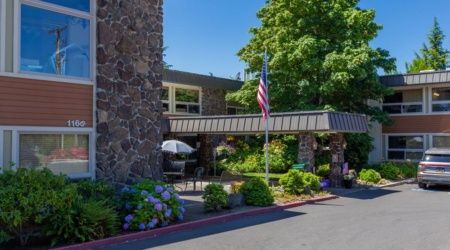 A building entrance with an American flag, surrounded by lush greenery and flowers.