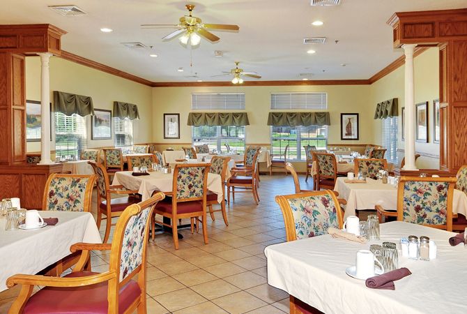 An empty dining area in a restaurant with neatly arranged tables and chairs, featuring large windows and decorative elements.