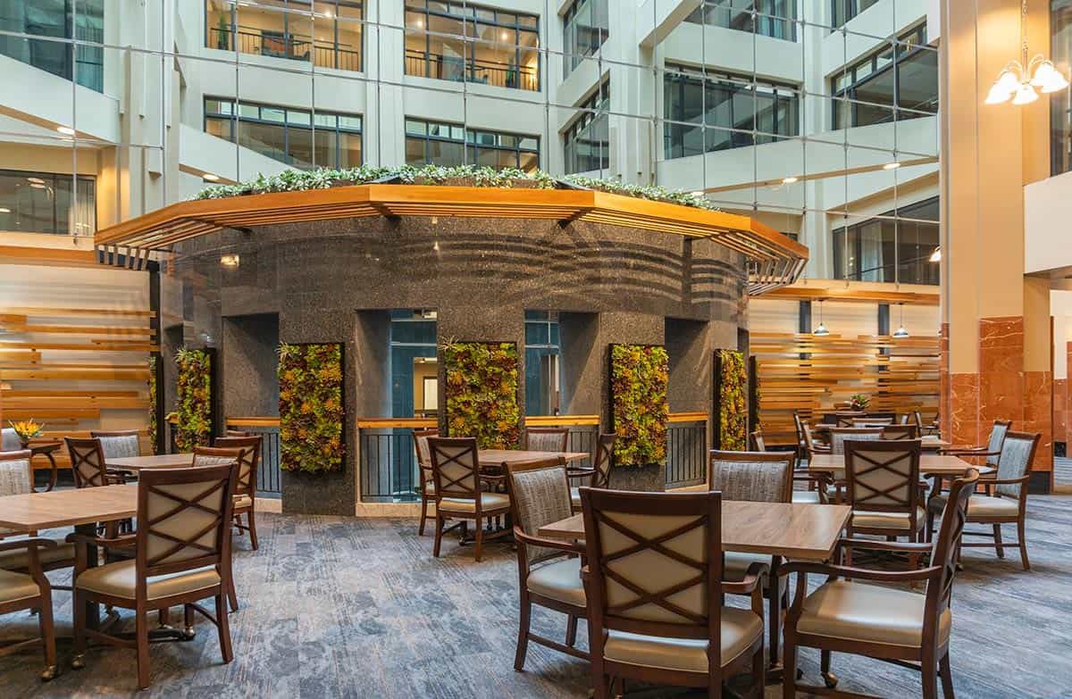 A modern indoor seating area with wooden furniture and greenery accents, located in a well-lit atrium.