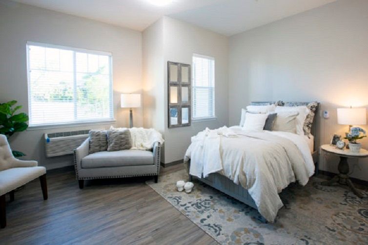 A modern and cozy bedroom with ample natural light, featuring a comfortable armchair and neatly made bed.