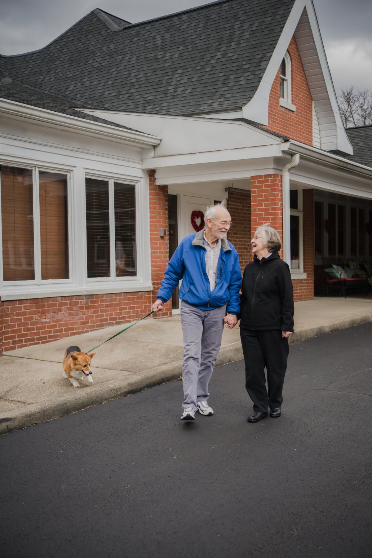An elderly couple taking a walk with their dog in a residential area.