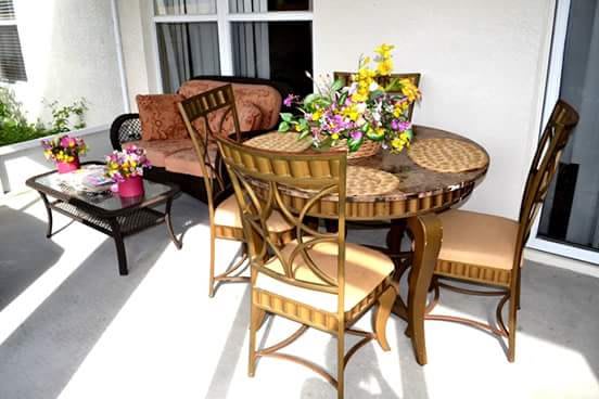A cozy outdoor patio setup with a wicker table surrounded by chairs, adorned with colorful flowers.