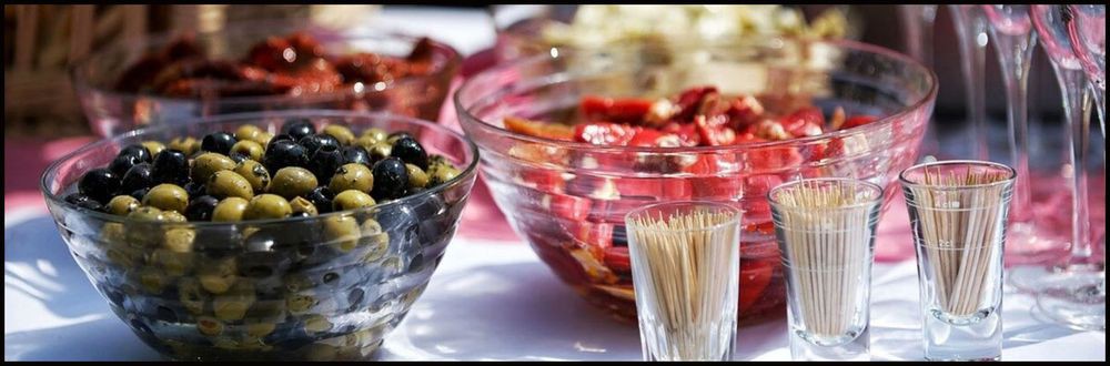 A selection of appetizers including olives and peppers, served in glass bowls with toothpicks.