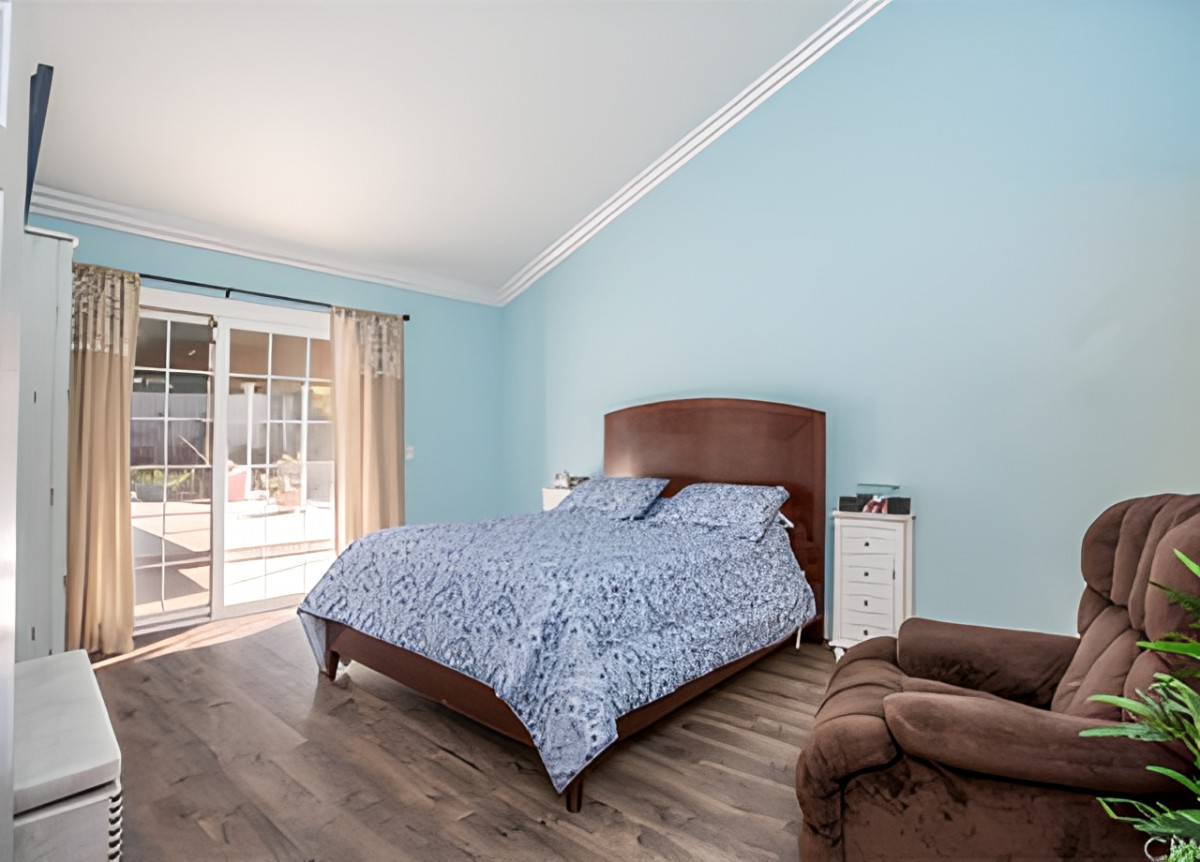 A cozy bedroom with blue walls, a bed covered in a patterned duvet, and natural light streaming through a sliding door.