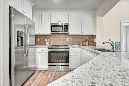 A beautifully designed modern kitchen featuring white cabinetry and sleek stainless steel appliances, complemented by a granite countertop and warm wooden flooring.