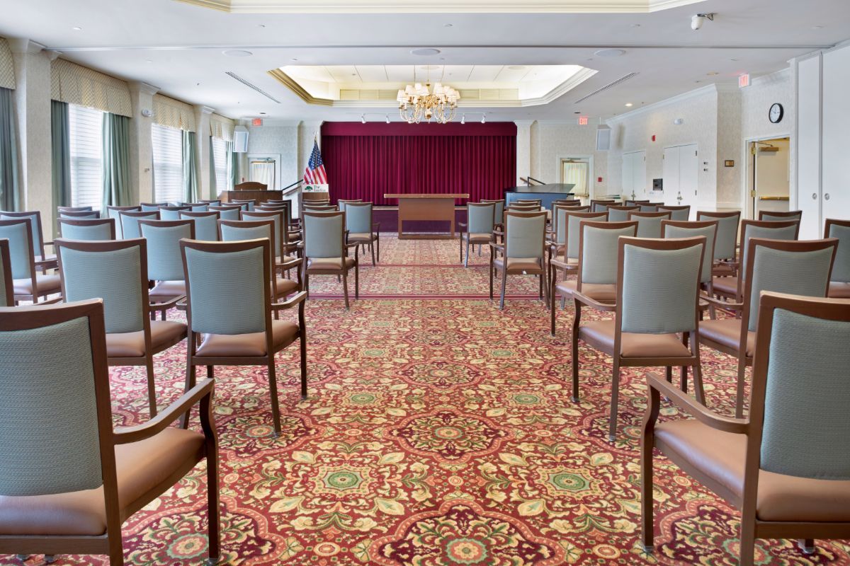 An empty auditorium with rows of chairs facing a stage with burgundy curtains.