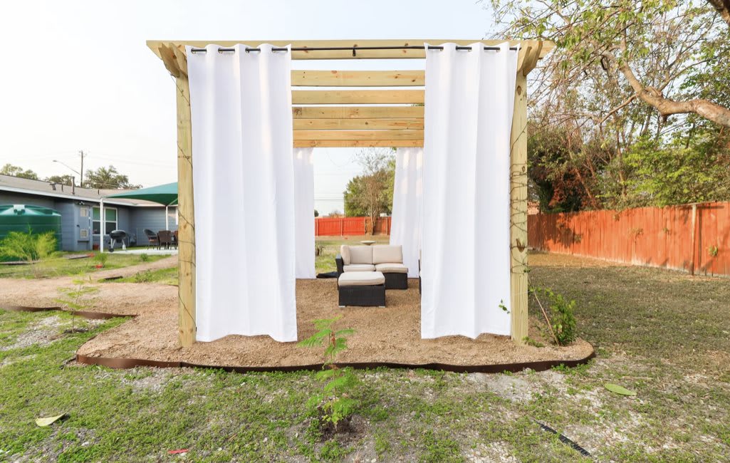 An outdoor pergola with white curtains and patio furniture.