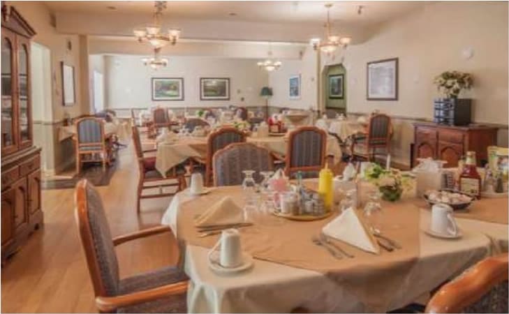 A warmly lit dining room with neatly arranged tables and chairs, featuring elegant chandeliers and a welcoming ambiance.