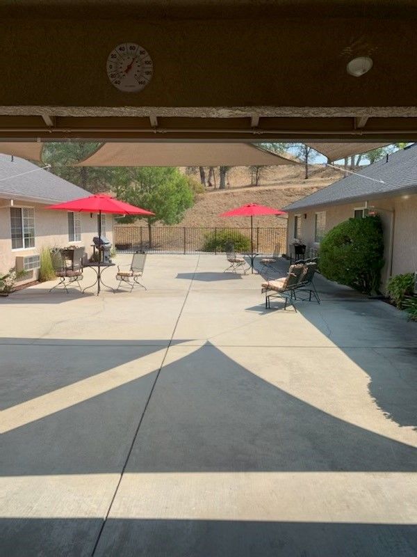 A sunny courtyard with outdoor seating, featuring red umbrellas and concrete flooring.