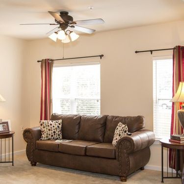 A cozy living room with a brown sofa, ceiling fan, and natural light streaming through the windows.