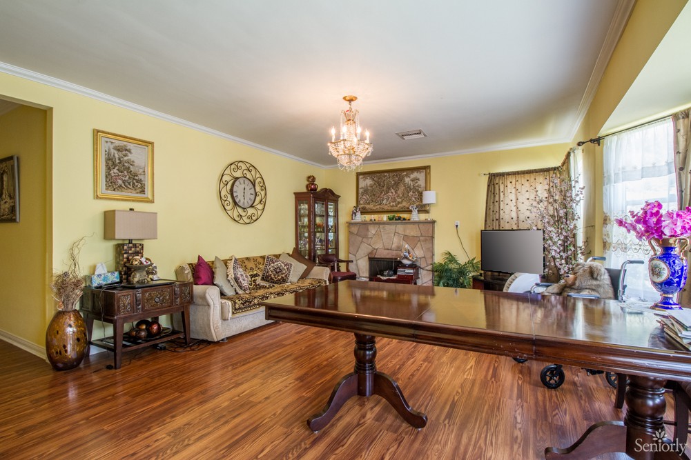 A traditional living room with wooden flooring, featuring a chandelier, sofa, table, fireplace, and cabinet.