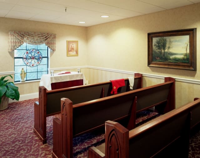 A small chapel inside a funeral home featuring wooden pews and paintings on the walls.