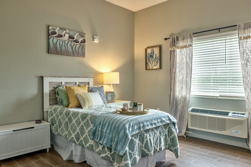 A cozy bedroom with a neatly made bed, soft lighting from a lamp, and decorative artwork on the walls.