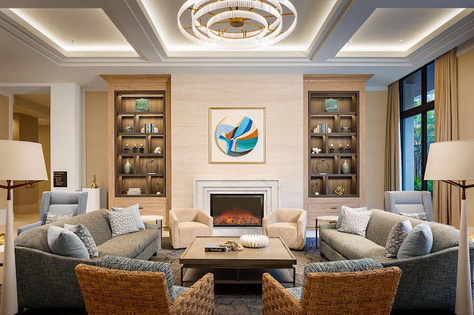 A modern living room featuring a central fireplace, surrounded by plush seating and elegant shelving, adorned with contemporary artwork and lighting.
