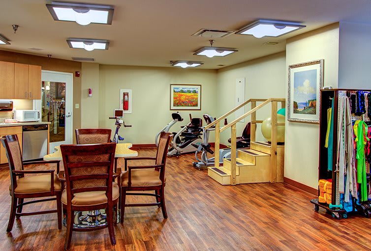 A cozy exercise room with gym equipment, wooden flooring, and seating area.