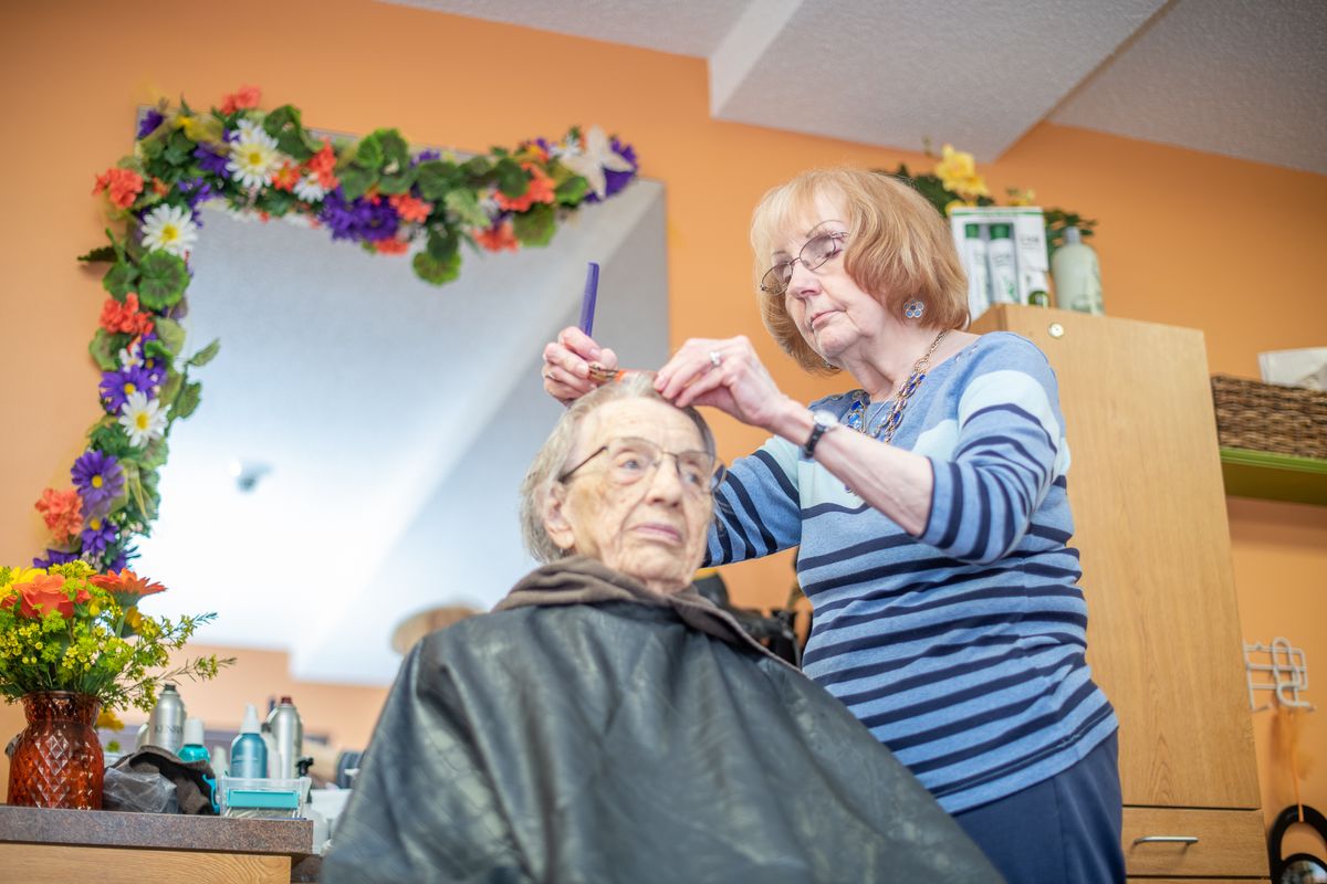 A hairdresser styling an elderly woman's hair in a salon.
