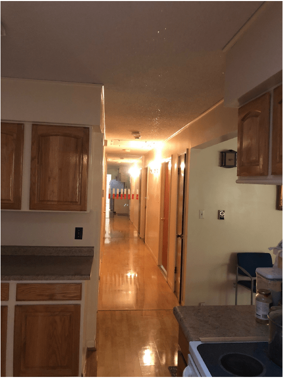 A view of a kitchen and hallway with wooden cabinets and flooring.