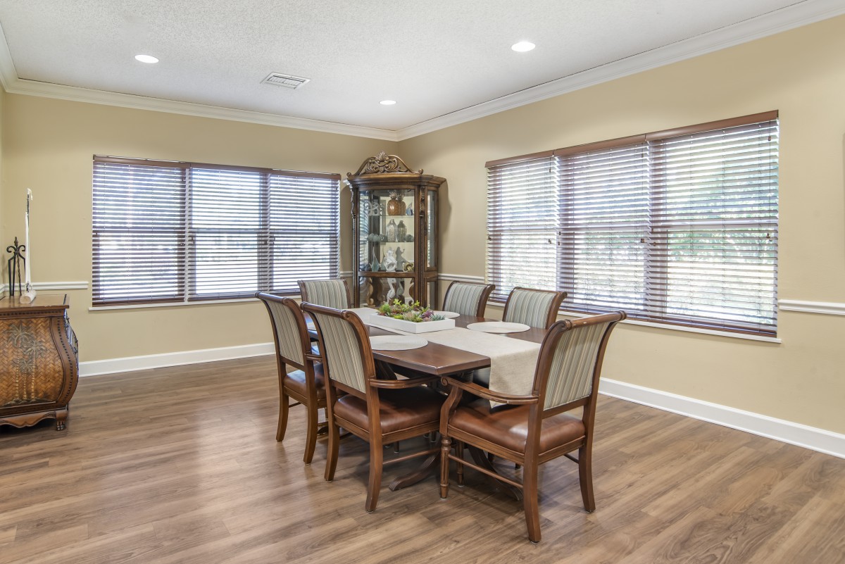 A well-lit dining room with a wooden table and six chairs, surrounded by large windows and featuring a hardwood floor.
