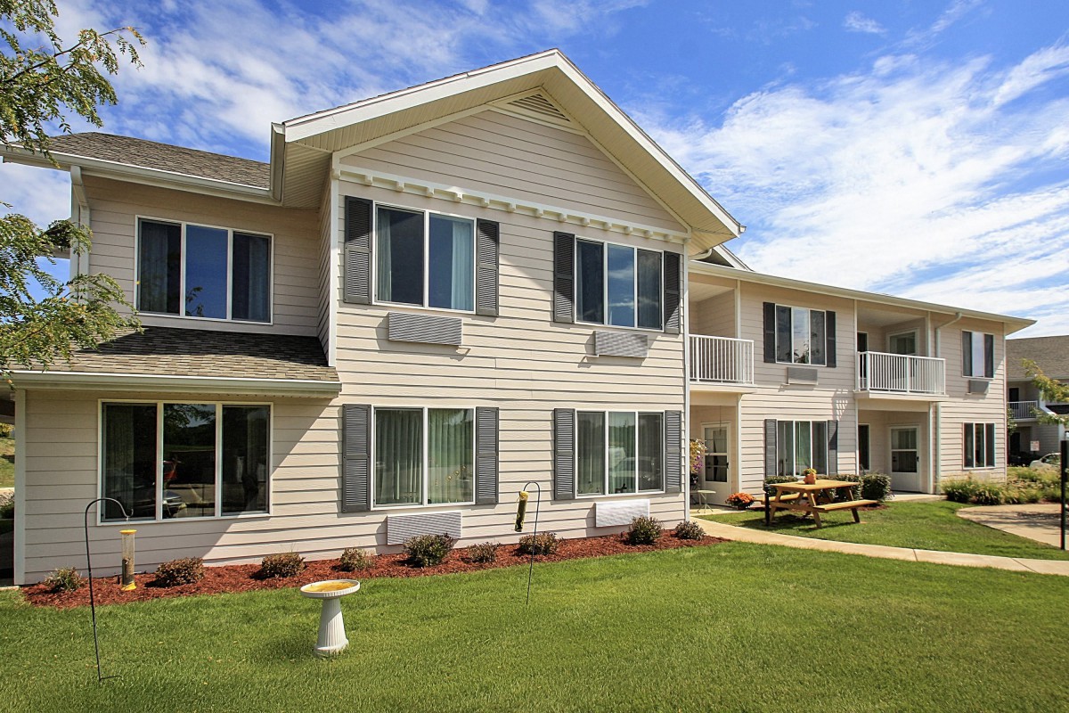 A two-story apartment building with beige siding and a well-maintained lawn on a clear day.