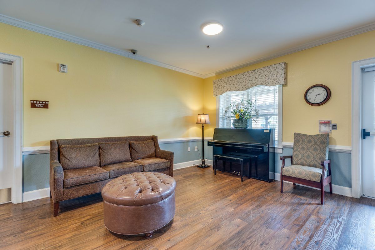 A cozy living room features a brown sofa, piano, and wooden flooring with soft lighting.
