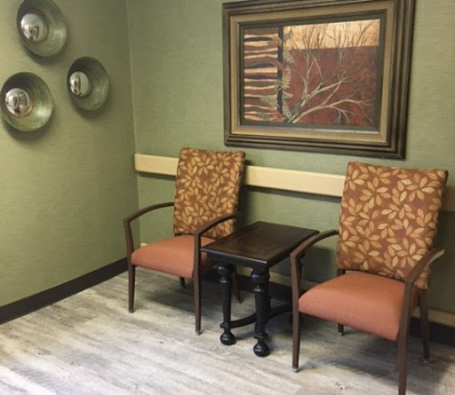 A cozy waiting area featuring two upholstered chairs and a small table, complemented by framed artwork on the wall.