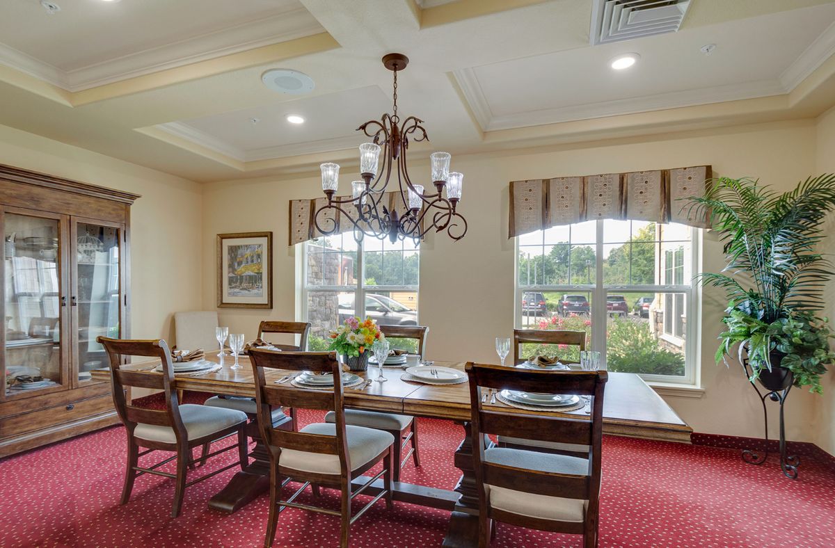 A well-decorated dining room with a large table, elegant chandelier, and abundant natural light.