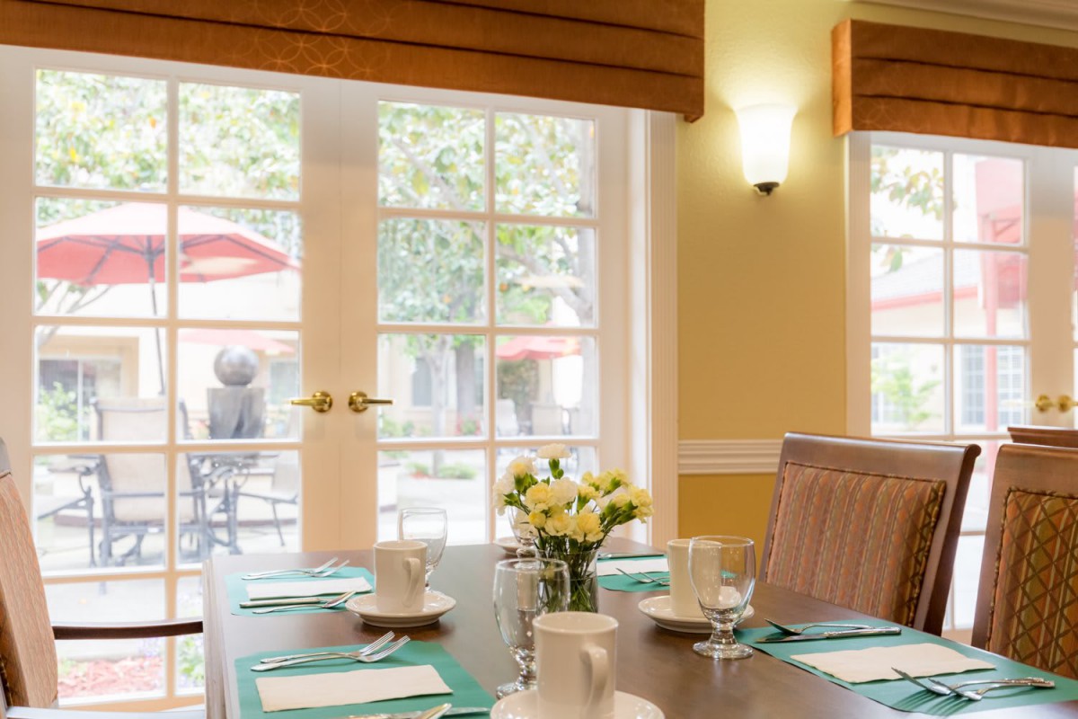 A cozy dining room with a neatly set table, featuring teacups and a vase of flowers by the window.