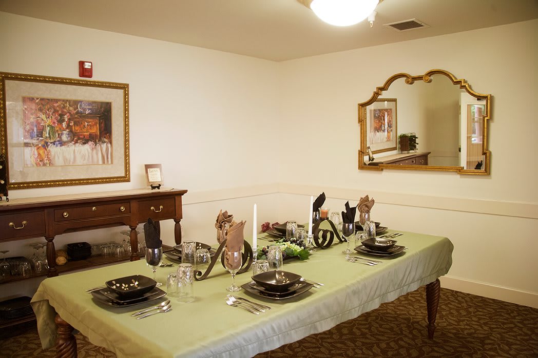 A dining room with an elegantly set table, featuring decorative plates, candles, and a mirror on the wall.