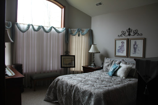 A cozy and elegant bedroom featuring a neatly made bed, soft color palette, and natural light streaming through large windows.