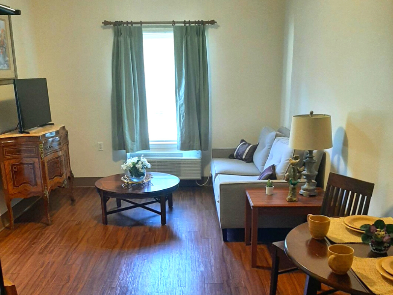 A cozy living room with a sofa and coffee table, framed by a window with curtains.