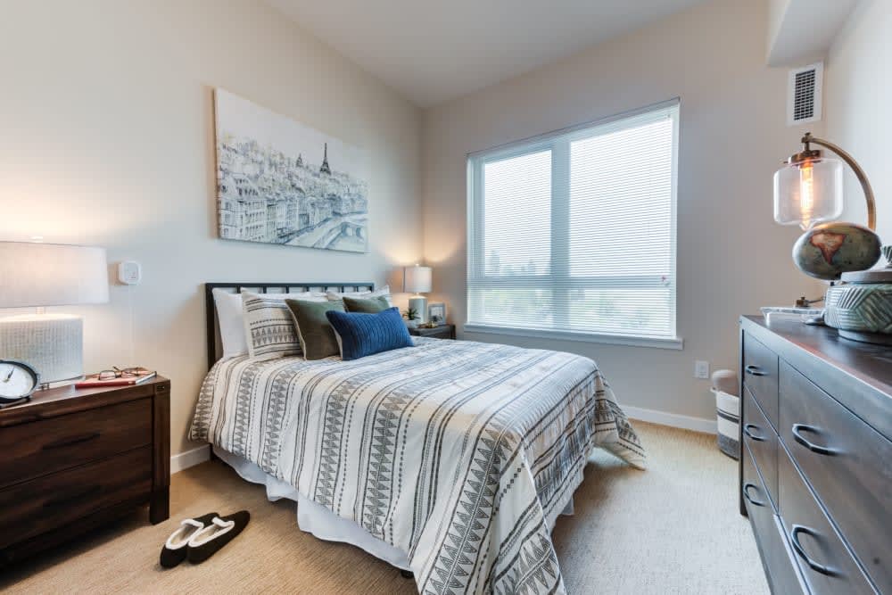 A cozy bedroom with a neatly made bed, large window, and stylish artwork.