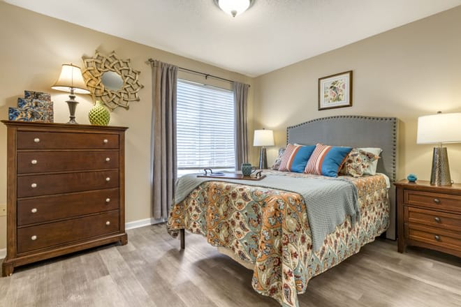 A cozy bedroom with patterned bedding, a wooden dresser, and a window with curtains.
