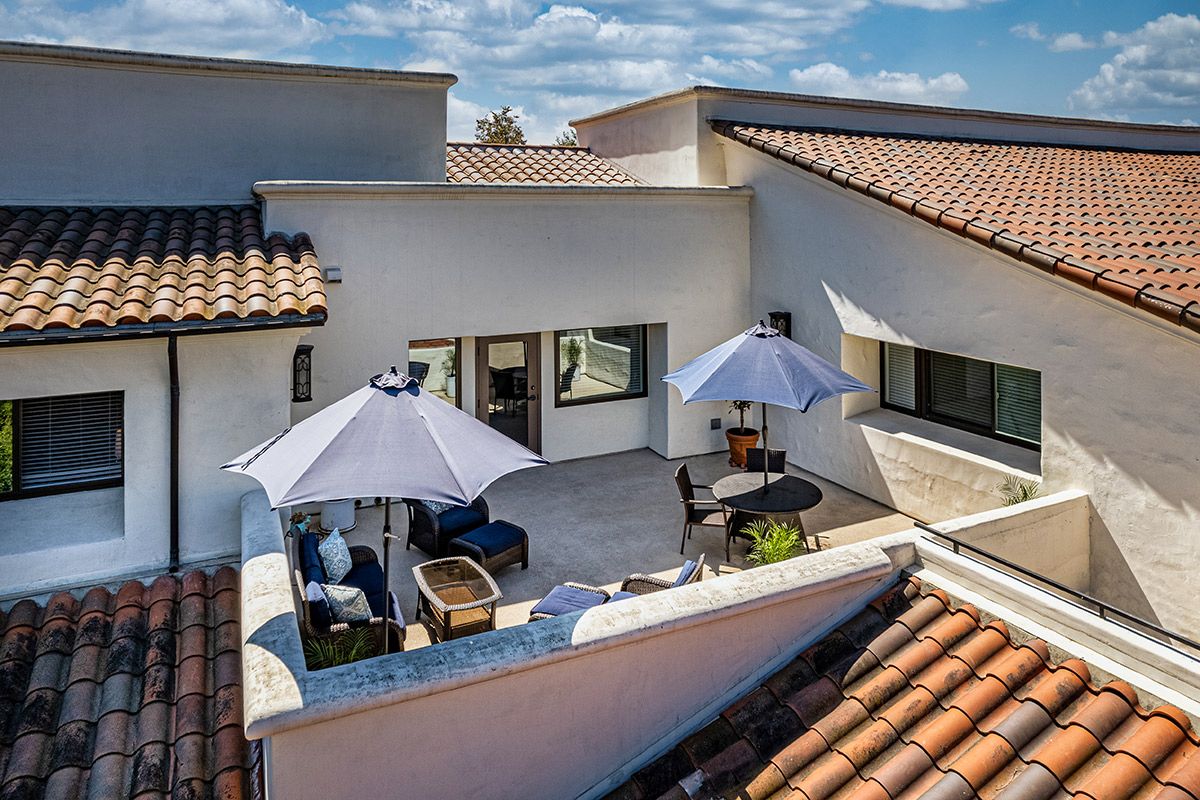 A sunny rooftop terrace with outdoor furniture and umbrellas on a modern building.