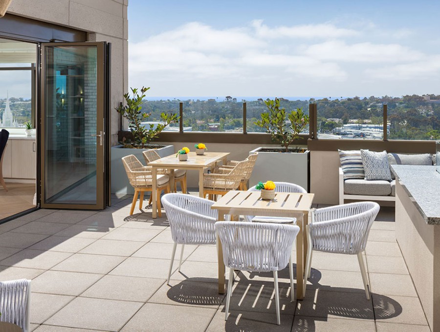 A rooftop terrace with tables and chairs overlooks the cityscape on a sunny day.