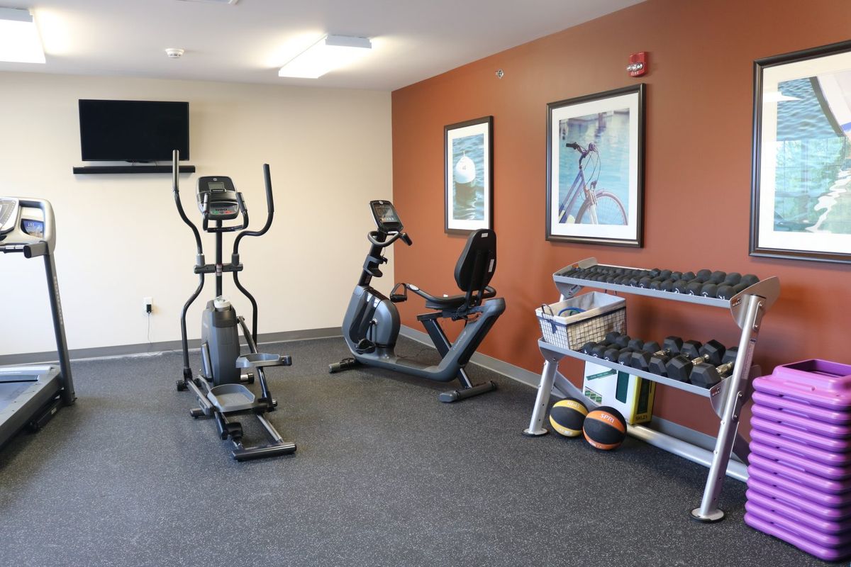 A small gym room featuring an elliptical machine, stationary bike, and a rack of dumbbells.