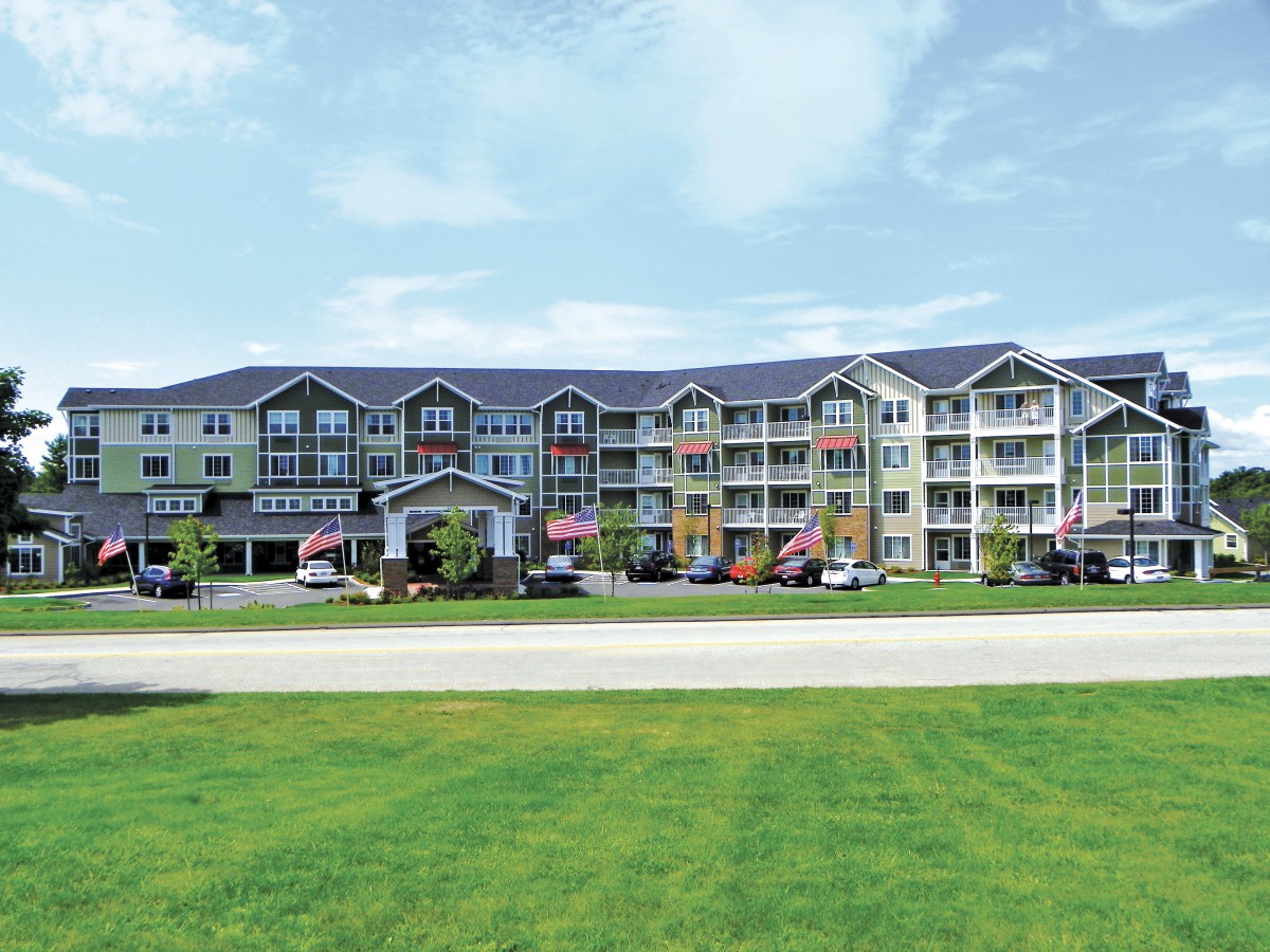 A multi-story residential apartment complex with a well-maintained lawn and clear skies.